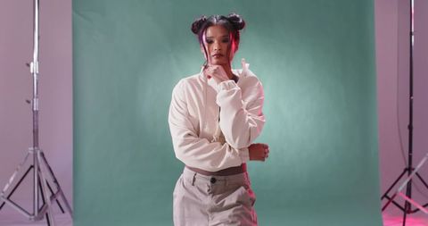 Asian woman posing in studio wearing hoodie and pendant against green seamless backdrop