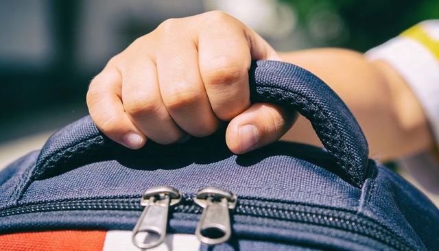 Child gripping backpack handle close-up showing small hand and zipper detail