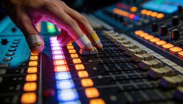 Adjusting mixing console faders with taped fingertips and illuminated led controls