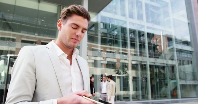 Young professional standing outside glass structured modern office building, concentrating on smartphone. Image suitable for business, corporate communication, technology use in urban settings, or work-life balance themes.