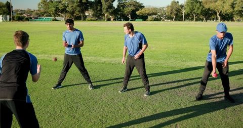 Male athletes practicing ball passing drill on green field outdoor team training session