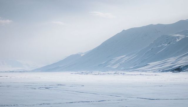 Silent arctic expanse stretching across frozen valley to distant frosted mountain ridges
