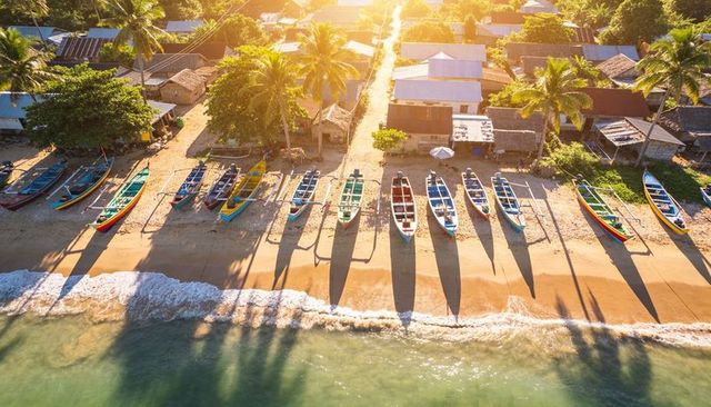 Colorful fishing boats lining sunlit tropical beach with long shadows at golden hour