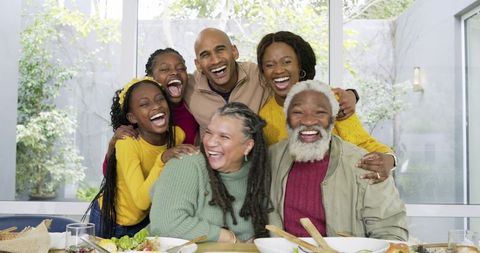 Multigenerational family laughing and sharing salad at sunlit dining table