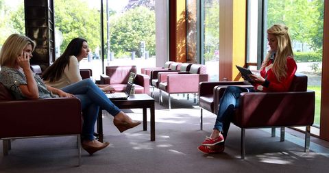 Three women in modern waiting room, each engaged in different activity