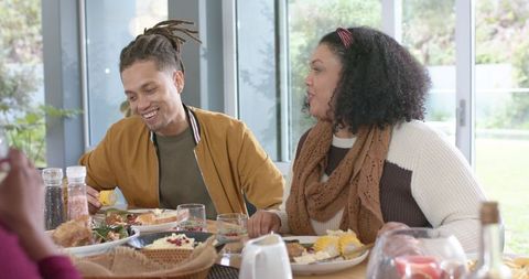 Diverse family sharing cozy home meal around table, laughing and chatting together