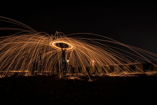 Person creatively spinning ignited steel wool at night creating beautiful, vibrant light patterns. Useful for backgrounds, desktop wallpapers, or marketing campaigns highlighting creativity, performance, or light displays.
