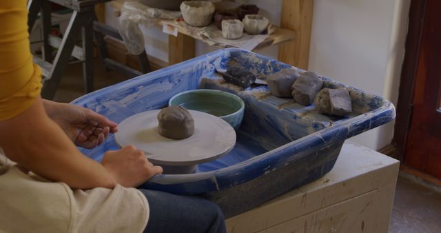 Person sculpting clay on spinning wheel in artisan workshop, showcasing craft and creativity. Suitable for hobbies, craftsmanship, traditional art, and ceramic making themes. Can be used in blogs, websites, or promotional content related to pottery, arts and crafts, handmade items, and creative processes.