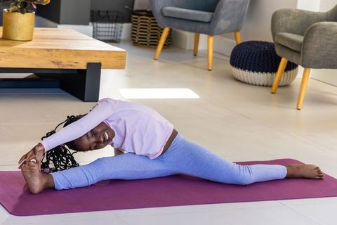 Sunlit african american teen girl stretching on purple yoga mat in modern living room