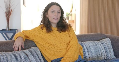 Relaxed woman wearing mustard sweater sitting on gray sofa in cozy minimalist lounge