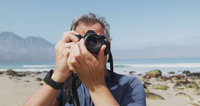 Senior man capturing moments on beach with DSLR camera. Represents outdoor hobby and passion for photography. Ideal for using in content related to travel, retirement activities, nature photography, and outdoor adventures.