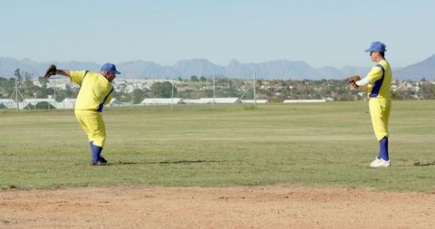 Two Male Teammates Throwing and Fielding on Sunny Baseball Field Wearing Yellow Uniforms