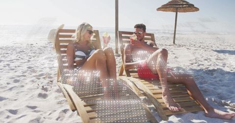 Couple relaxing on sunlit beach chairs sipping cocktails, wearing sunglasses, tropical seaside escap