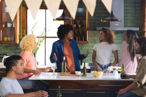 Friends chatting and sharing drinks around kitchen island during casual home gathering