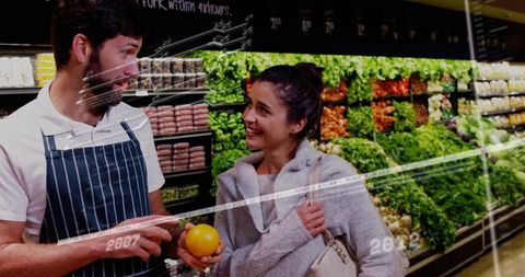 Grocery clerk explaining orange to smiling shopper in produce aisle
