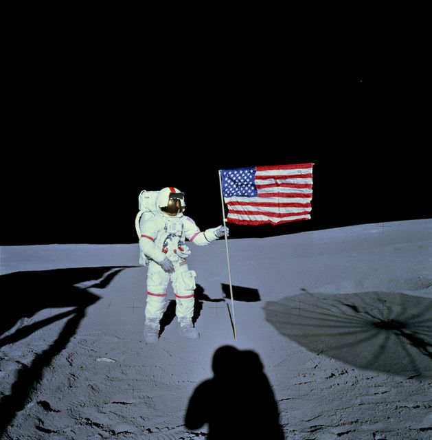 AS14-66-9232 (5 Feb. 1971) --- Astronaut Alan B. Shepard Jr., commander of the Apollo 14 lunar landing mission, stands by the deployed United States flag on the lunar surface during the early moments of the first extravehicular activity (EVA) of the mission. Shadows of the Lunar Module (LM), astronaut Edgar D. Mitchell, lunar module pilot, and the erectable S-Band Antenna surround the scene of the third flag implanting to be performed on the lunar surface. While astronauts Shepard and Mitchell descended in the LM ?Antares? to explore the Fra Mauro region of the moon, astronaut Stuart A. Roosa, command module pilot, remained with the Command and Service Modules (CSM) ?Kitty Hawk? in lunar orbit.