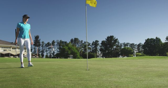 Woman golfer wearing blue shirt, white pants, and a visor standing on a green under a clear sky. Golf flag and trees visible in background. Perfect for illustrating outdoor sports, recreational activities, summer sports, and promoting golf courses.