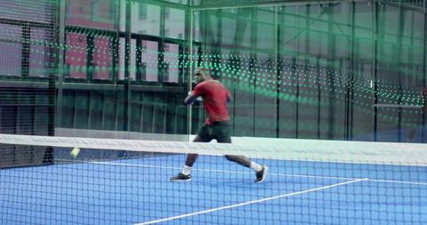 Male player hitting backhand on blue indoor court during fast tennis rally