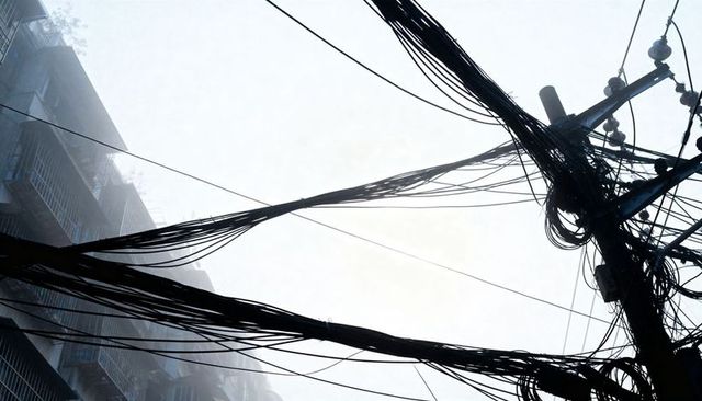 Tangled overhead utility cables crossing narrow urban alleyway with apartment balconies