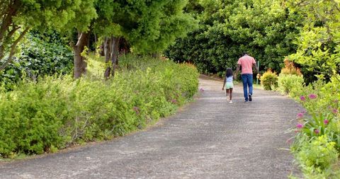 Father and Daughter Strolling Garden Path Under Lush Trees