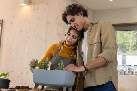 Happy couple planting herb seedlings in modern kitchen