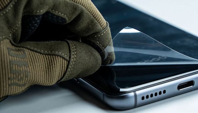 Gloved hand peeling screen protector from smartphone close-up with port reflection usb-c