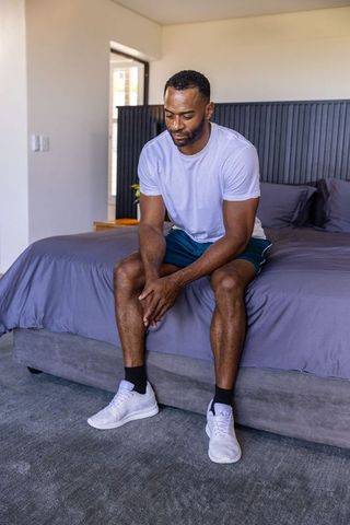 Mature african american man sitting on bed edge, clasping hands, contemplative morning