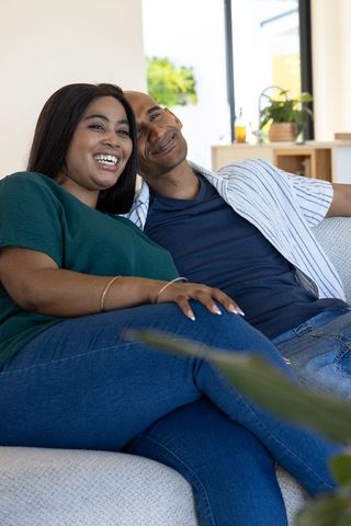 African american couple relaxing and smiling on minimalist sofa in bright living room