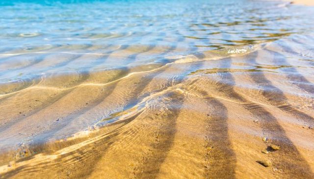 Sunlit shallow seawater revealing golden sand ripples and shimmering turquoise shoreline
