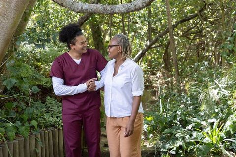 Caregiver holding hands with african american senior woman walking through lush garden