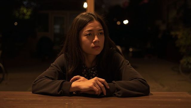 Young woman reflecting at night on wooden table under warm bulb light