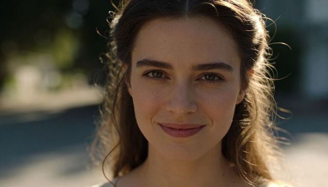 Smiling young woman gazing into camera with golden hour backlight and natural beauty portrait