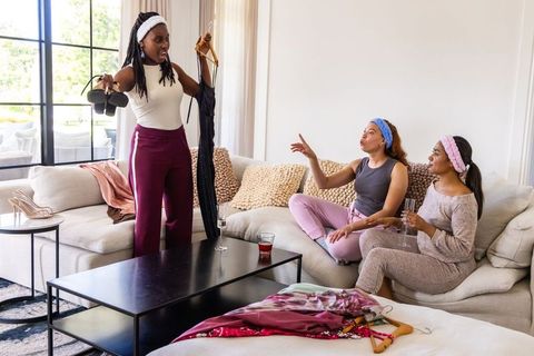 African american friends trying on dresses and heels at home, styling outfits and laughing