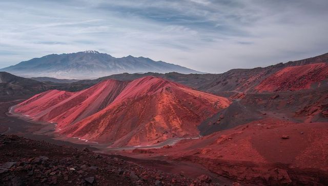 Crimson volcanic ridges in arid highland valley with winding dirt track and rocky scree