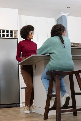 African american mother leaning at kitchen island talking with daughter on bar stool