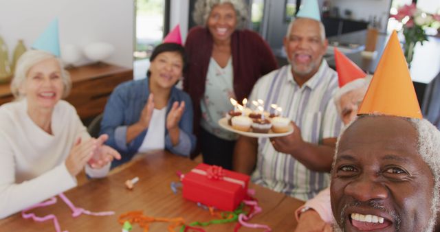 Portrait of happy senior diverse people at birthday party with cake and gifts at retirement home. healthy, active retirement and body inclusivity.