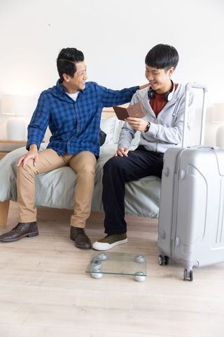 Asian father and son checking passport on bed with suitcase before trip