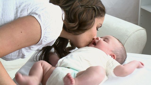 This captures a warm moment of a mother showering love and affection on her baby with a gentle kiss at home. Useful for family and parenting themes, depicting nurturing relationships and emotional connections in caregiving activities.