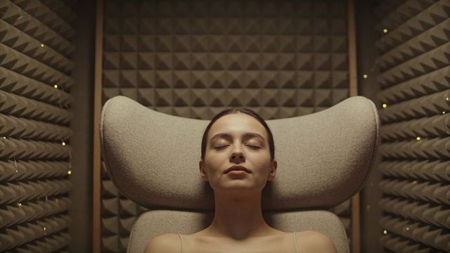 Woman relaxing in soundproof listening booth with ambient string lights and high-back chair