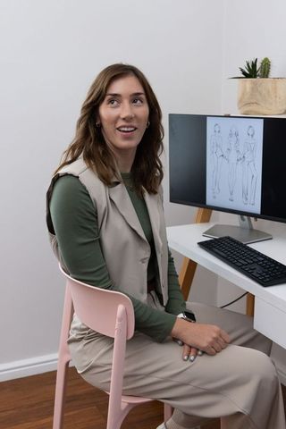 Fashion illustrator reviewing sketches in minimal home studio with pastel palette