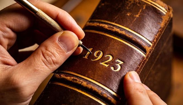 Restoring antique leather book spine tooling and gold gilding hands working 1923