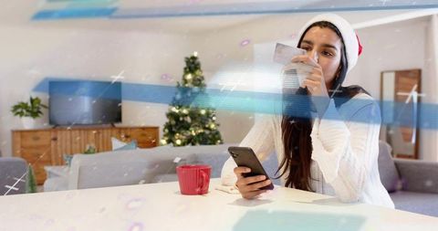 Woman in santa hat holding smartphone and credit card for online holiday shopping at home