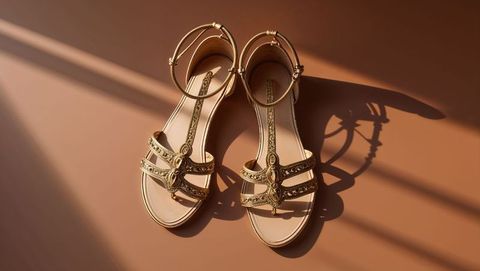 Ornate gold-tone women's sandals on sunlit surface