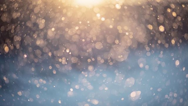 Sunlit bokeh particles glittering over blue snow blur with warm golden dreamy highlights