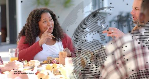 Woman in red cardigan speaking at sunny brunch with friends, pastries and dotted glass partition