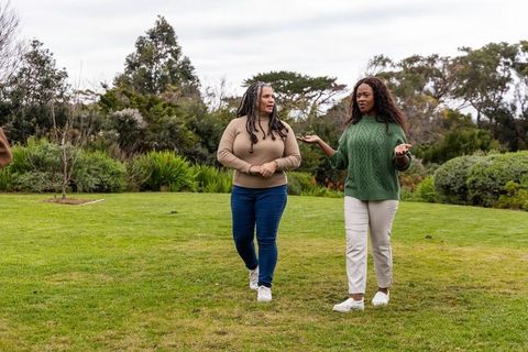 Two african american women walking and talking in park wearing sweaters and sneakers