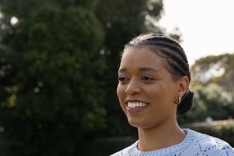 African american woman smiling blue sweater with gold hoops, cornrow bun outdoor headshot