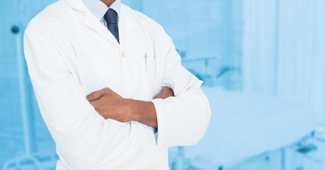 Male doctor wearing white coat and stethoscope standing with arms crossed in a hospital setting. Great for use in healthcare advertising, medical-related articles, blogs on health and wellness, or hospital brochures to convey professionalism and confidence.