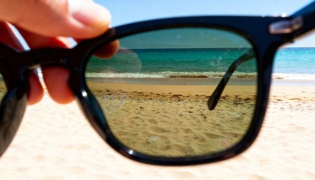 Hand Holding Sunglasses Framing Turquoise Beach Through Tinted Lenses for Summer Travel