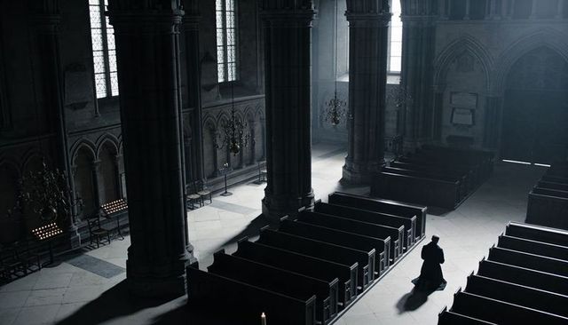 Solitary cleric kneeling in gothic cathedral nave with dramatic sunlight and empty pews